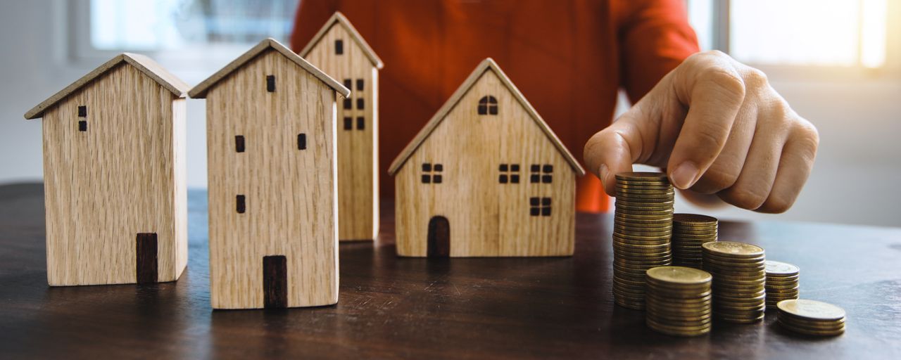 ours-journey Planning investments with stacked coins and model houses on a table.